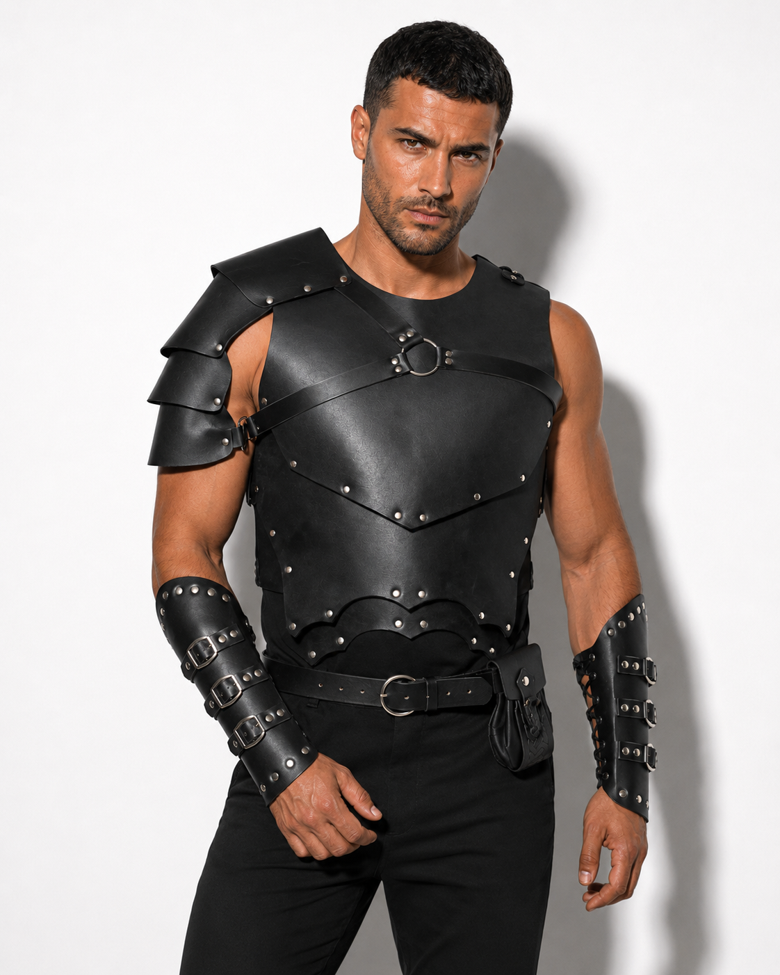 A man modeling a black faux-leather armor costume set with a chest plate, shoulder guards, a belt, and matching arm bracers against a white studio background.
