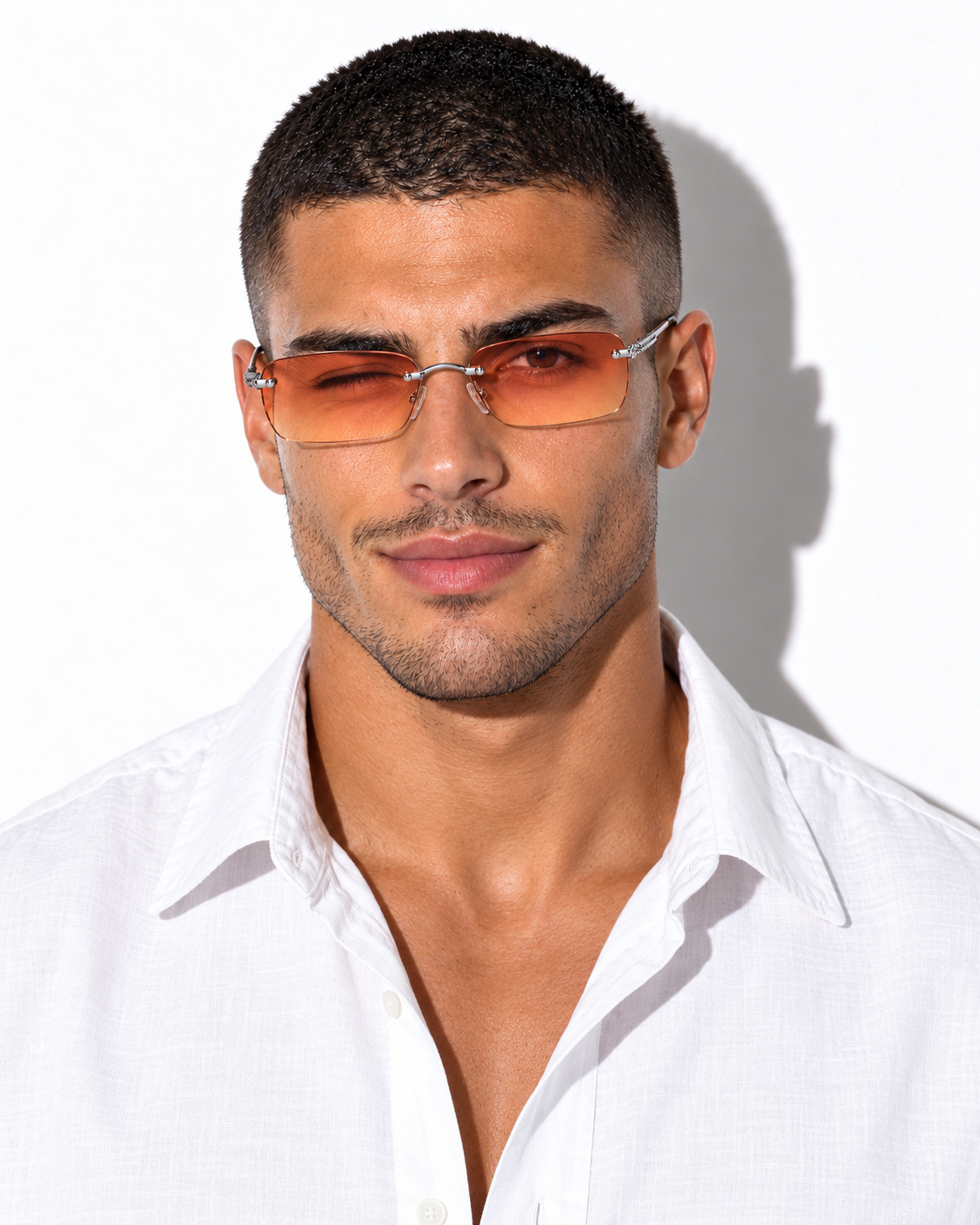 A man wearing rectangular tinted orange sunglasses with a thin silver metal frame and a white button-down shirt, photographed against a white background with a hard shadow.