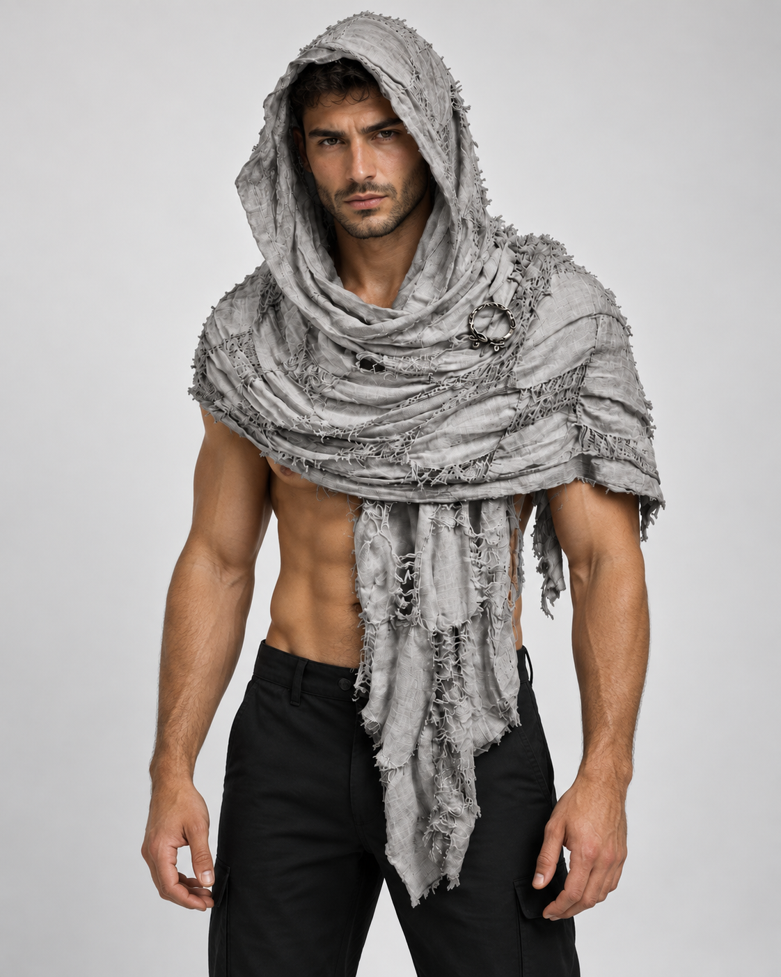 A muscular man modeling a distressed, frayed gray hooded scarf or shawl wrapped around his shoulders and head, paired with black pants, against a light gray studio background.