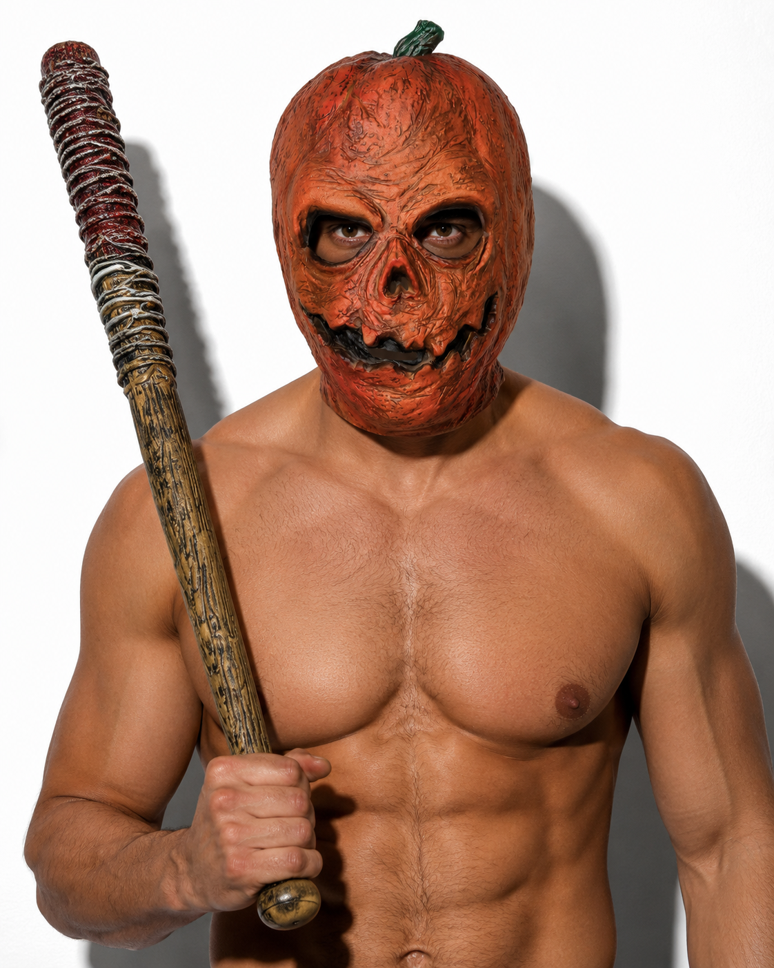 A shirtless man wearing a textured orange pumpkin mask with a green stem and holding a baseball bat, photographed against a plain white background.