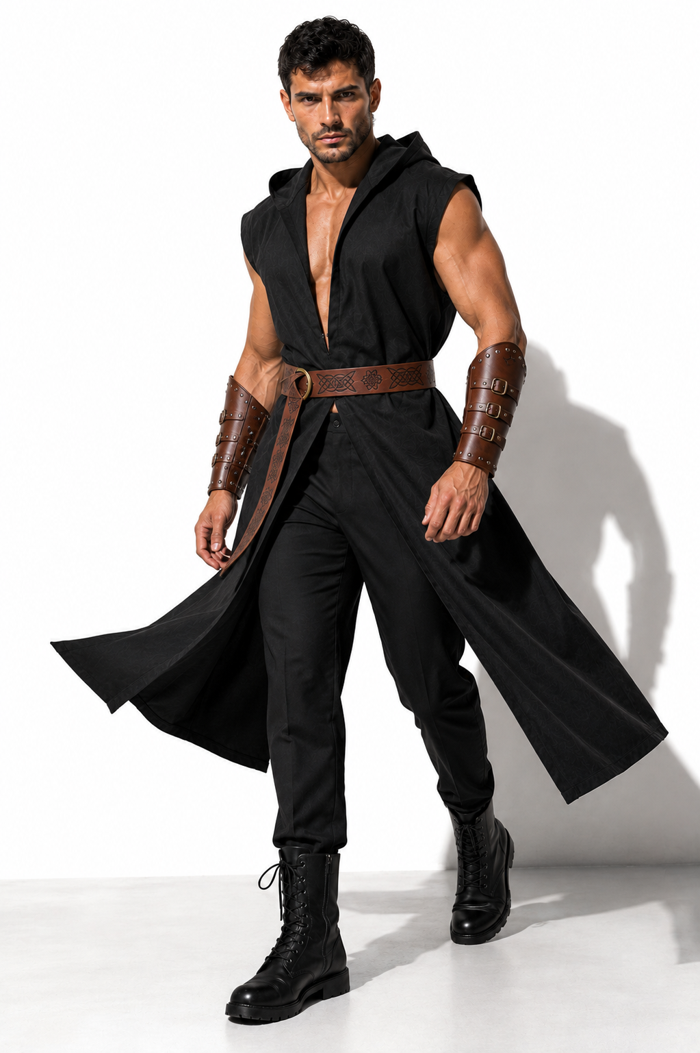 A muscular man modeling a black hooded costume vest with a long flowing drape, a brown belt, matching brown arm bracers, black pants, and black combat boots against a white studio background.